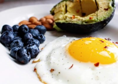 Fried egg on a white plate with an avocado and blueberries